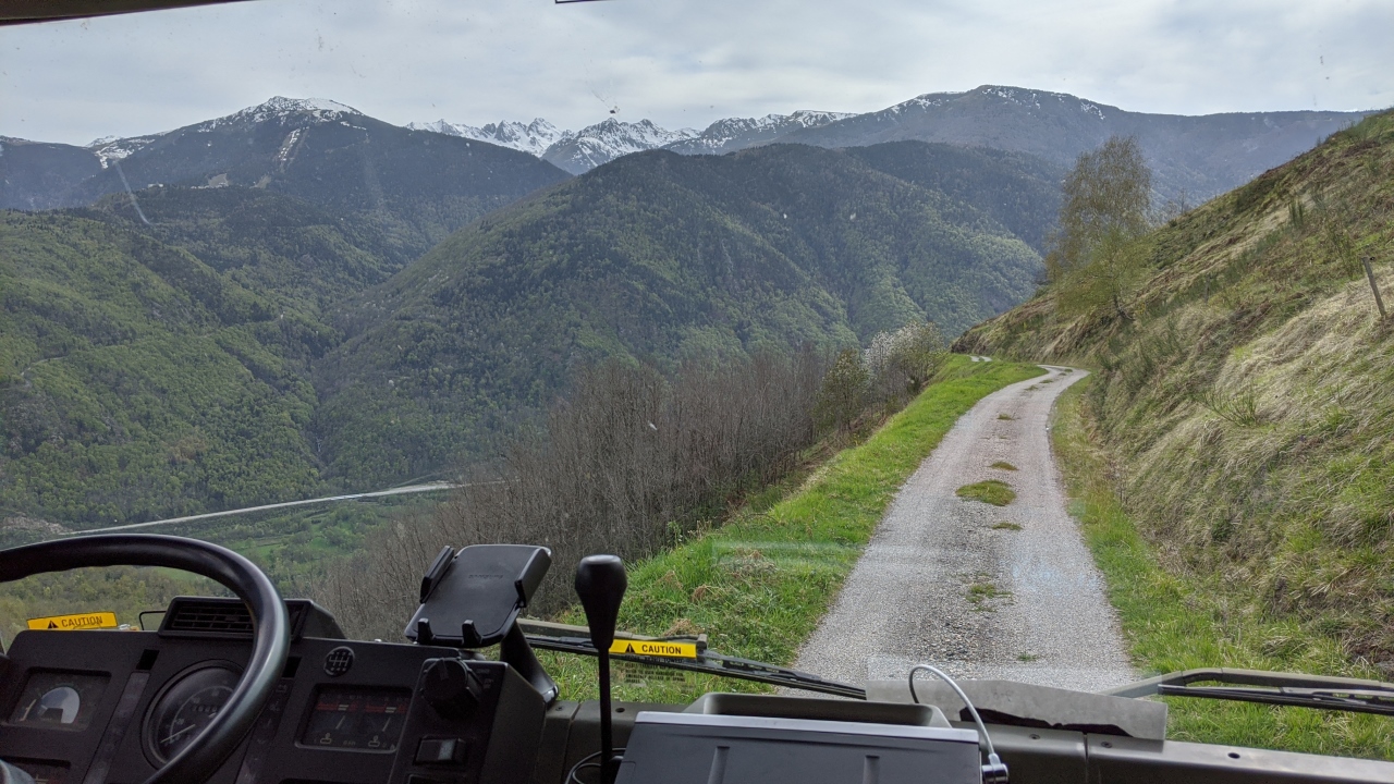 Blick aus dem Cockpit vom Truck auf einen sehr engen Feldweg, der eigentlich zu klein für das Fahrzeug ist. Im Hintergrund sind schneebedeckte Berge. 