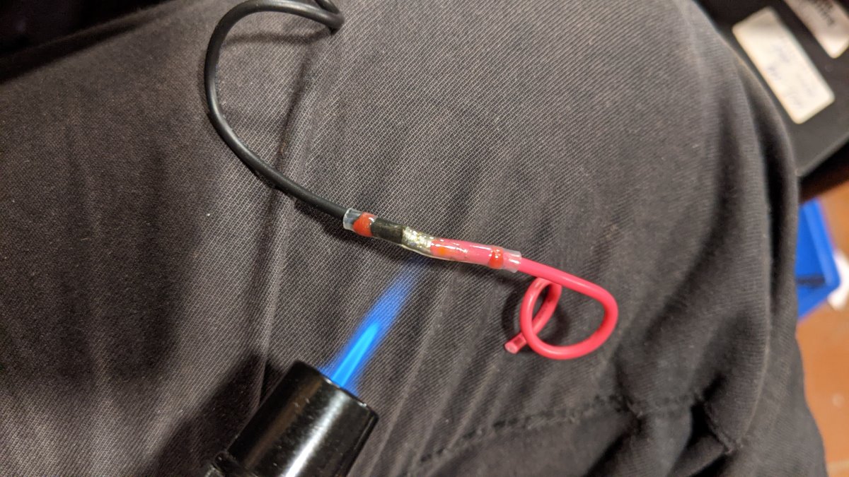 Ein Jetfeuerzeug erhitzt einen Lötverbinder Schnellverbinder um ein rotes und ein schwarzes Kabel dauerhaft zu verbinden 