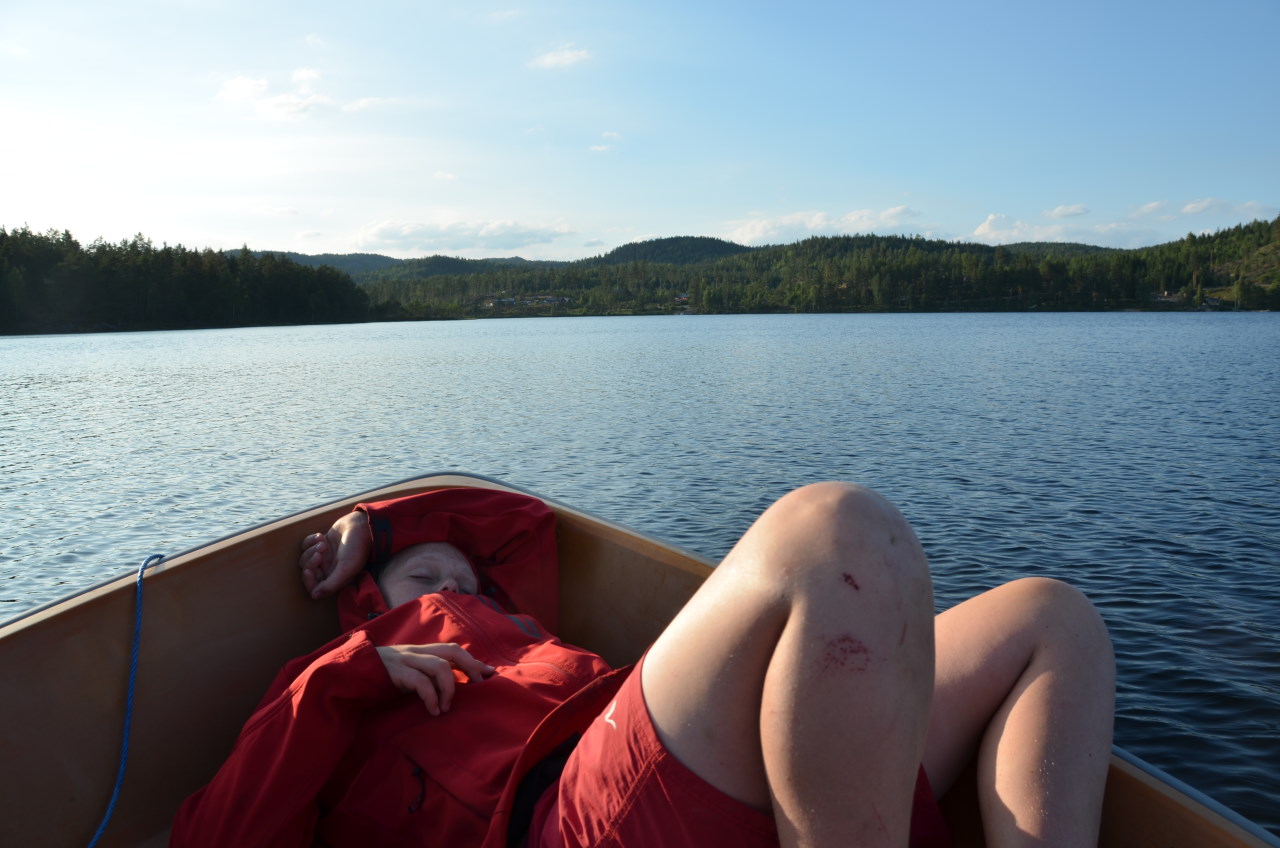 Kind mit roter Regenjacke liegt faul in einem Ruderboot