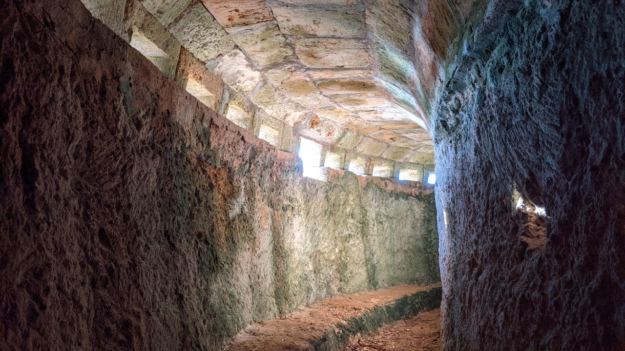 Innenansicht eines Bunkers am Strand. Die Sonne scheint durch die kleinen Schiessscharten und erhellt den Innenraum etwas. 