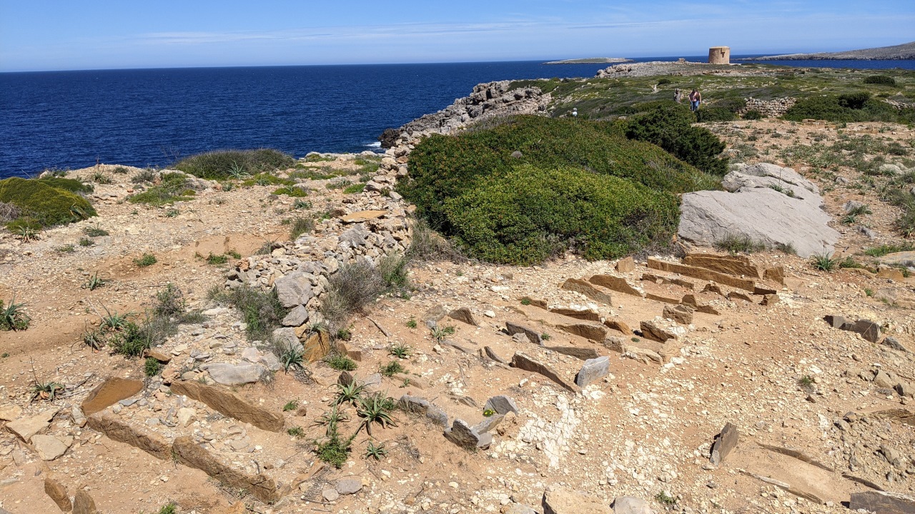 Ein römischer Friedhof in Cape Cavalleria auf Menorca, das Bild zeigt Gräber am Rande des blauen Meers