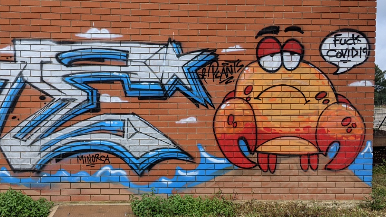 Ein Wand Graffiti in Menorca. Zu sehen ist ein Cartoon mit einem Krebs der fuck covid 19 ruft.  