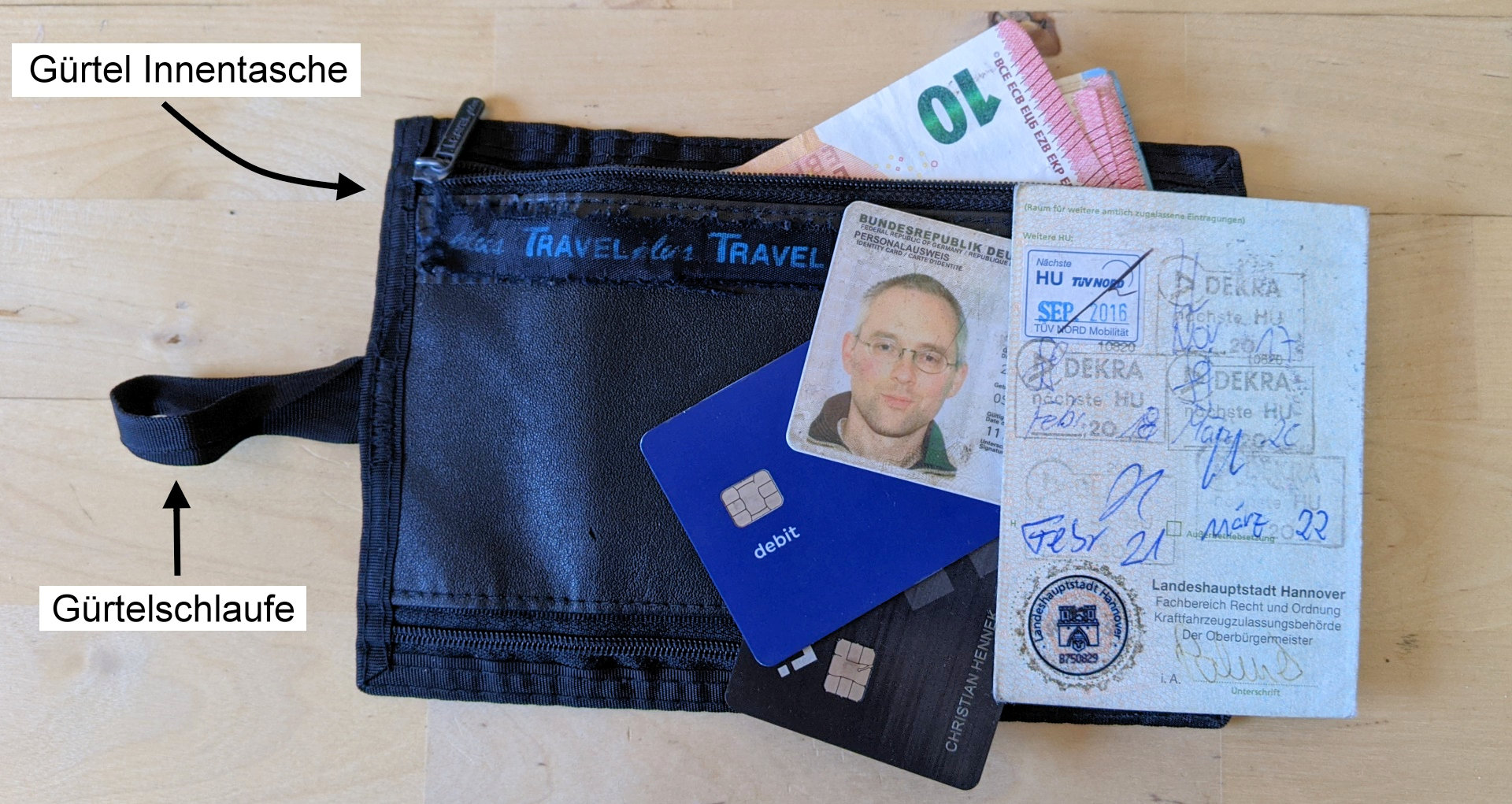 Gürtelinnentasche, der Inhalt ist auf der abgelegten Tasche abgebildet: ein Perso, zwei Kreditkarten, Fahrzeugpapiere und etwas Bargeld