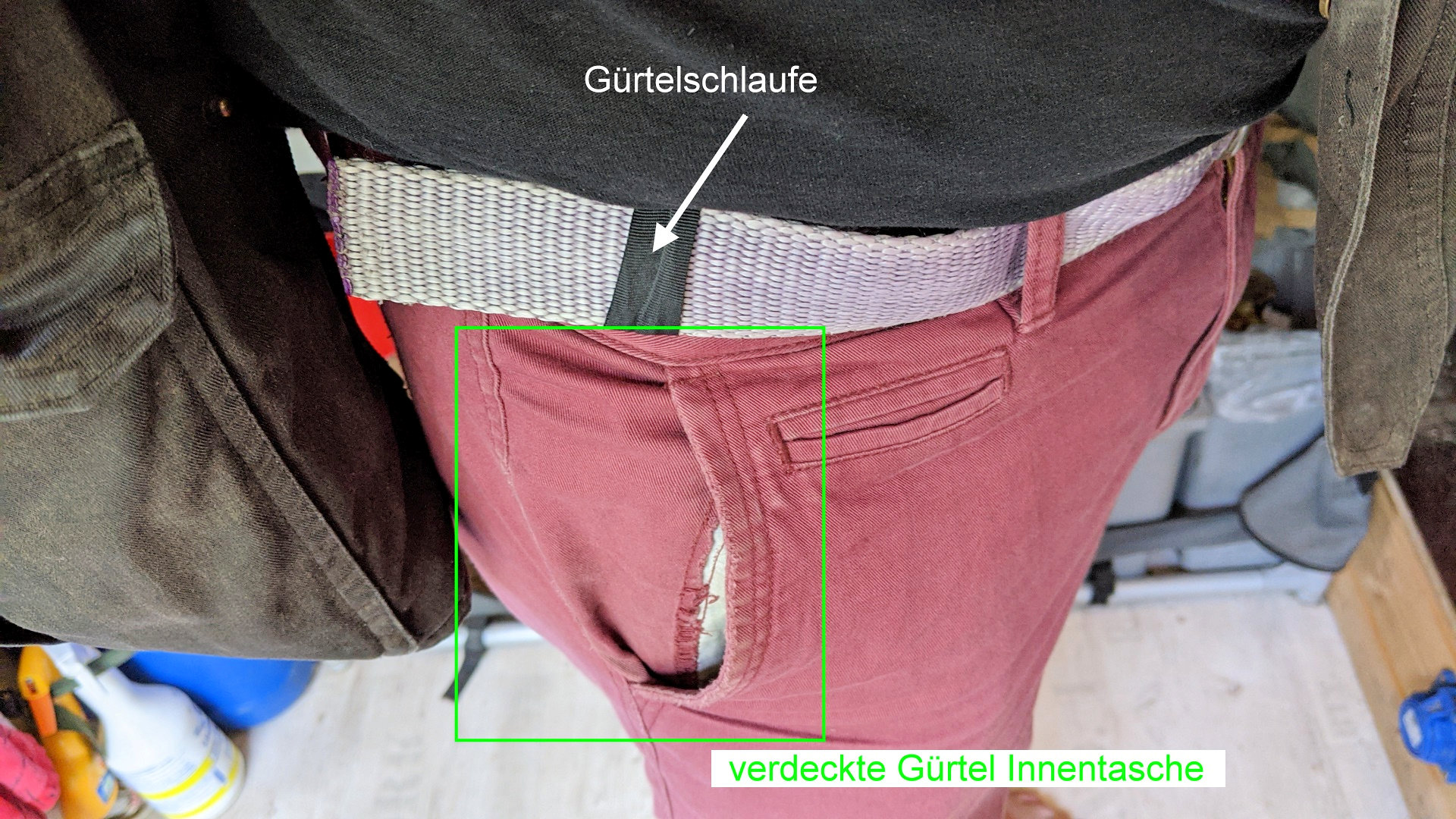 Auf dem Bild ist eine Person, die am Gürtel eine Innentasche befestigt hat. Die Gürtelinnentasche ist in die Hose gesteckt worden und nicht zu sehen. Das vorhandensein der Tasche erkennt man nur daran, dass eine schwarze Lasche am Gürtel hängt im Gegensatz zu weinroten Laschen der getragenen Hose. 