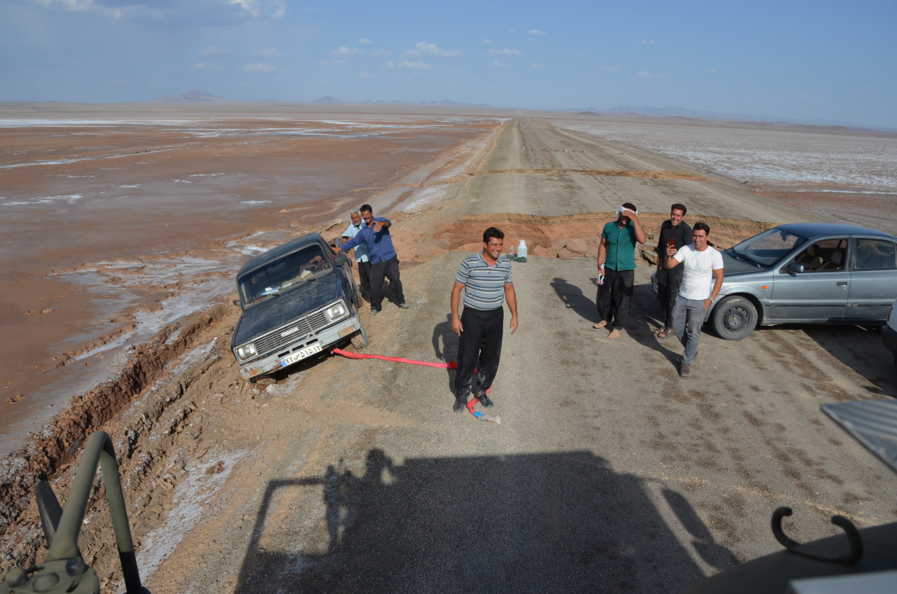 Ein Mazda Pickup wird im Iran aus dem Schlamm gezogen. Mehrere Menschen stehen auf einem Damm. 