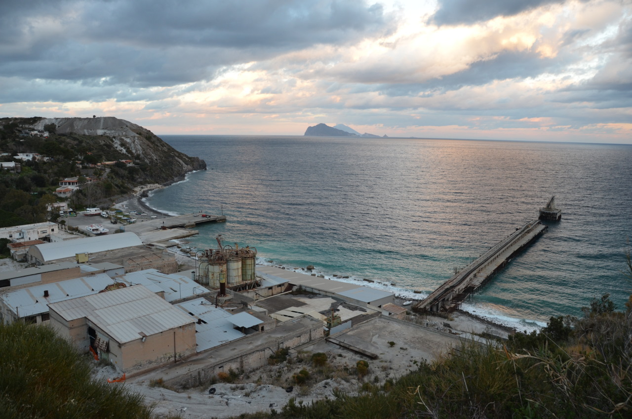 Luftbild der aufgegebenen Bimssteinfabrik von Lipari mit fabrikhallen und dem halb verfallenen Anleger. Im Hintergrund ist das Meer und die Inseln Stromboli und Panarea zu sehen. 