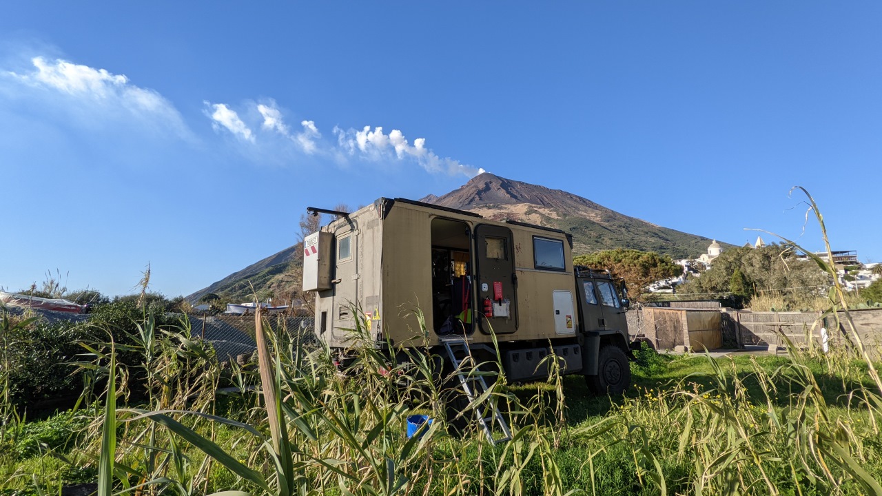 Der DAF T244 Truck in Stromboli, auf dem Grundstück von Emanuel geparkt. Der Vulkan ist im Hindergrund vom Bild und stößt kleine Rauchwolken aus die nach links wehen. 