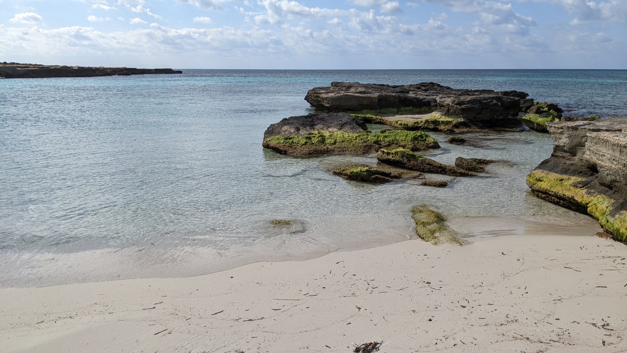 Der Lido Burrone Strand in Favignana. Das Bild zeigt das blaue Meer, Felsen und den hellen Sandstrand. 