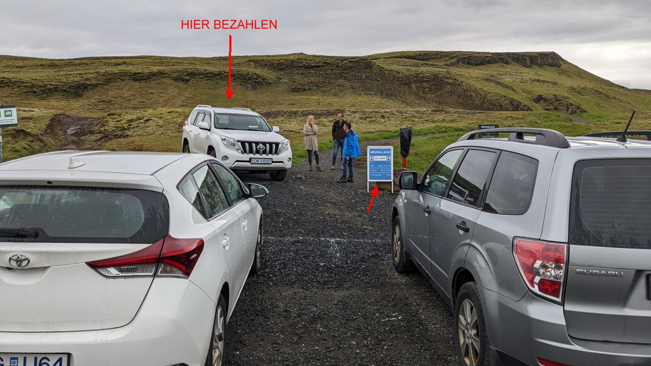 Mehere Autos parken vor dem Naturbad Hrunalaug. Rote Pfeile weisen auf das Auto hin, wo der Landbesitzer kassiert und ein blaues Schild mit den Eintrittspreisen.  