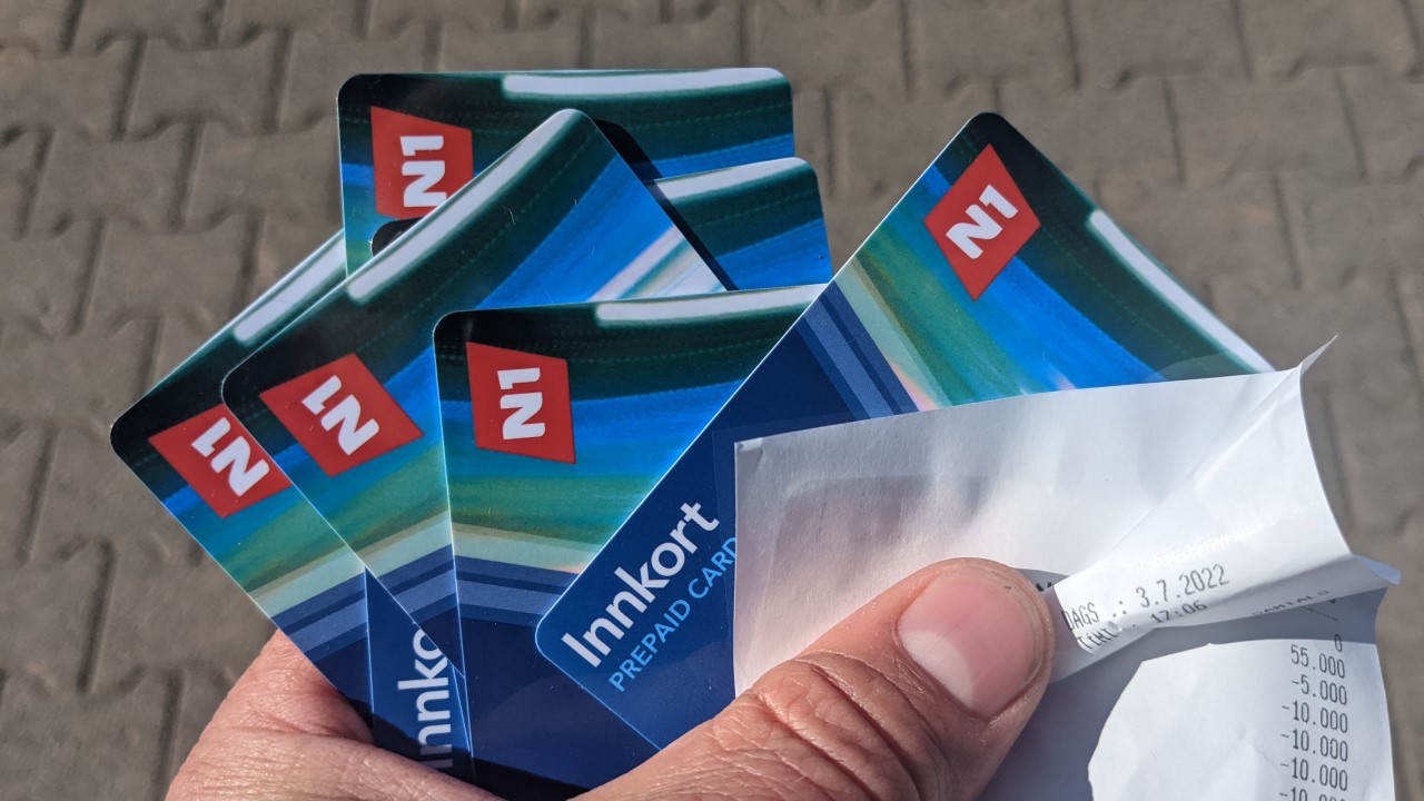 Eine Hand hält 6 blaue Guthabenkarten vom Anbieter N1 und eine Papier Quittung fest. Auf einer Guthabenkarte aus Plastik ist die Beschriftung Innkort prepaid card zu sehen. 
