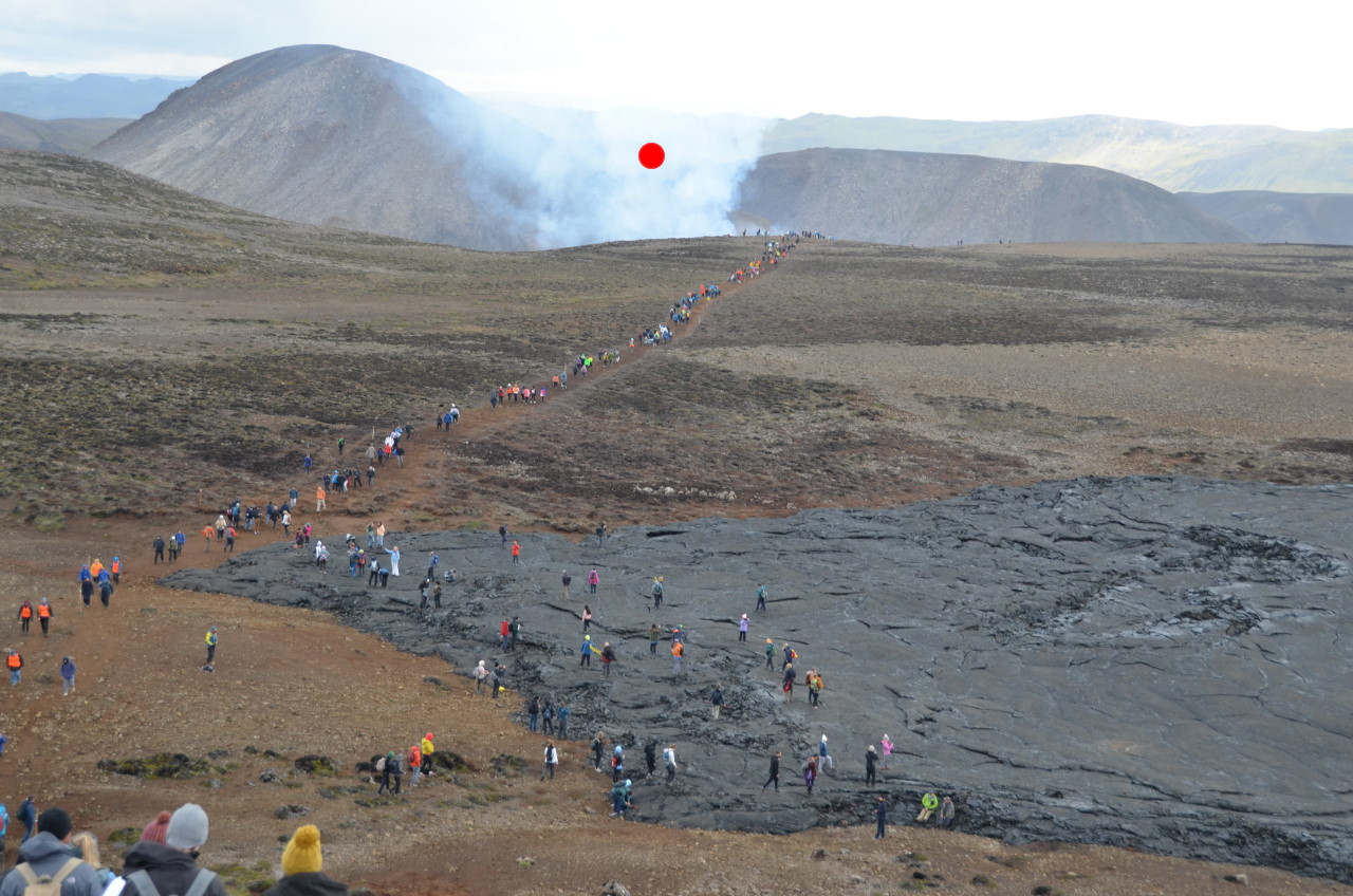 Eine lange Schlange von Touristen wandern zum Vulkanausbruch Fagradalsfjall vom Auguste 2022 in Island. Im Hintergrund ist Rauch vom aktiven Vulkan zu sehen, dieser ist mit einem roten Punkt als Wegweiser  markiert. 