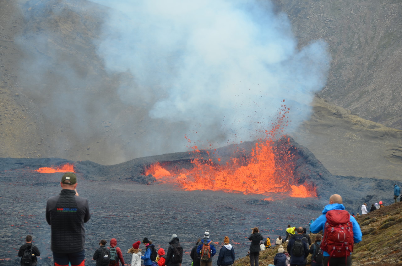 Der Meradalir Vulkan in Island spuckt Lava, im Vordergrund betrachten Zuschauer den Vulkanausbruch