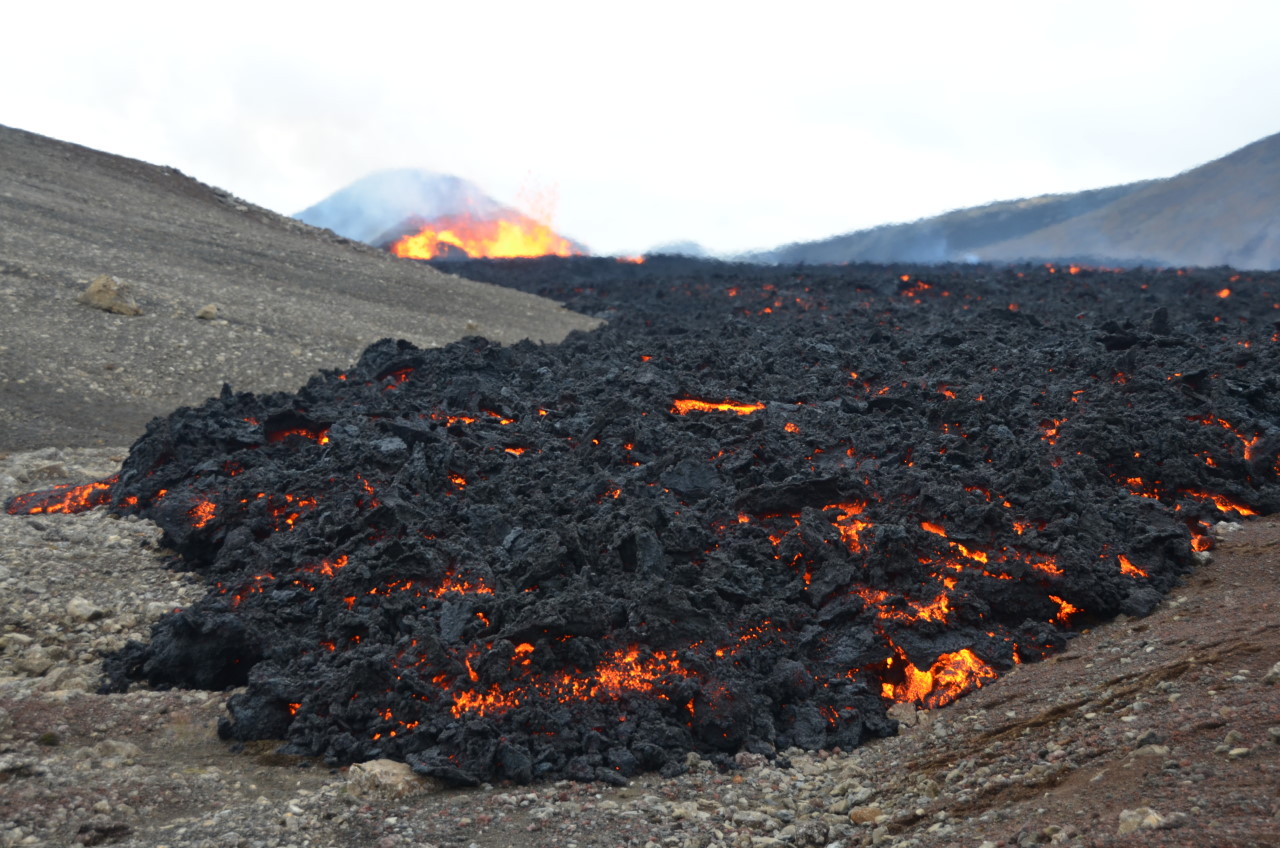 Eine erkaltete Lava Walze im Tal, wischen der schwarzen Schlacke glüht rote Lava. 
