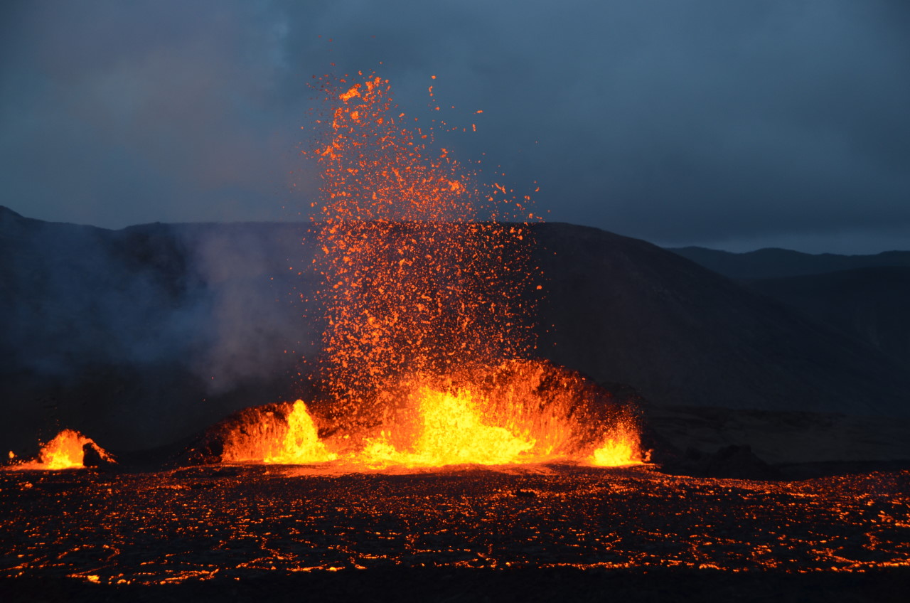 Der Meradalir Vulkan Fagradalsfjall spuckt nachts rot glühende Lava. In unteren Teil des Bildes ist ein Lava See mit schwarzen Lavaplatten zu sehen 