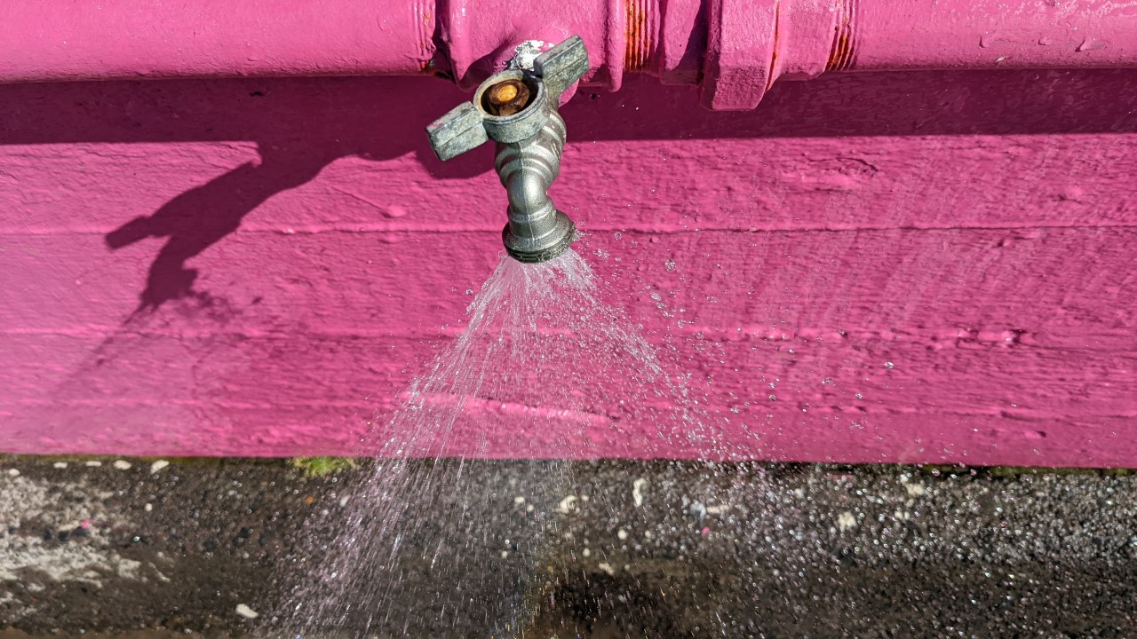 Ein Wasser in alle Richtungen verspritzender Wasserhahn vor pinkem Hintergrund