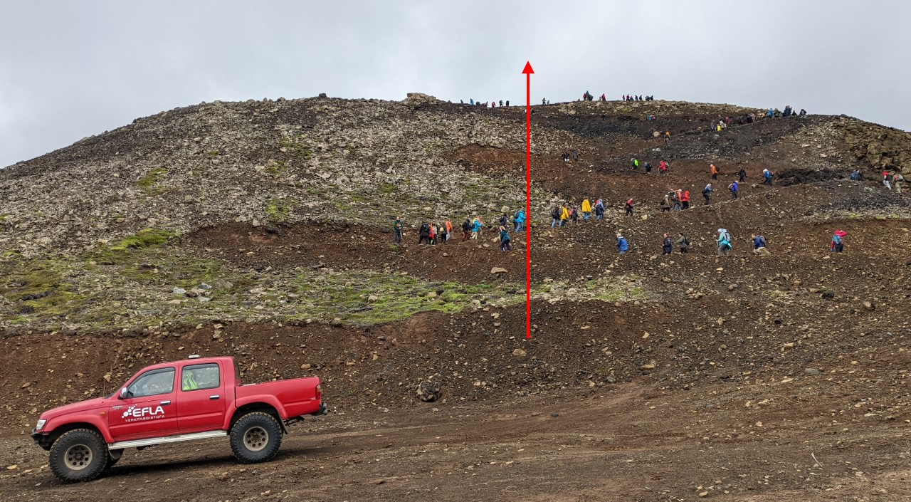 Besucher vom Vulkanausbruch Fagradalsfjall steigen einen Berg hoch, im Vordergrund parkt ein roter Geländewagen. 