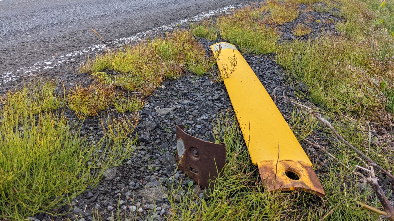 Eine gelbe Begrenzungsbarke aus Plastik liegt am Strassenrand. Neben der Barke ragt ein scharfkantig aussehendes Blechstück aus dem Boden. 