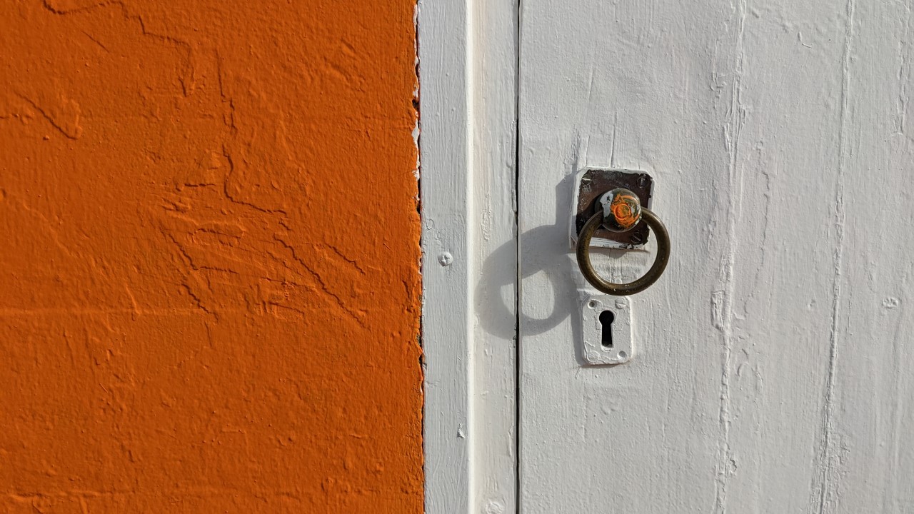 Detail Aufnahme von einer weiss gestrichenen Tür neben einer orangenen Wand