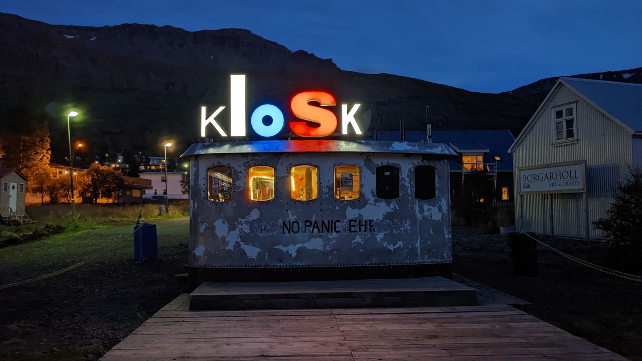 Nachtaufnahme einer kleinen Verkaufsbude, die ein beleuchtetes Schild mit dem Wort Kiosk auf dem Dach hat. 