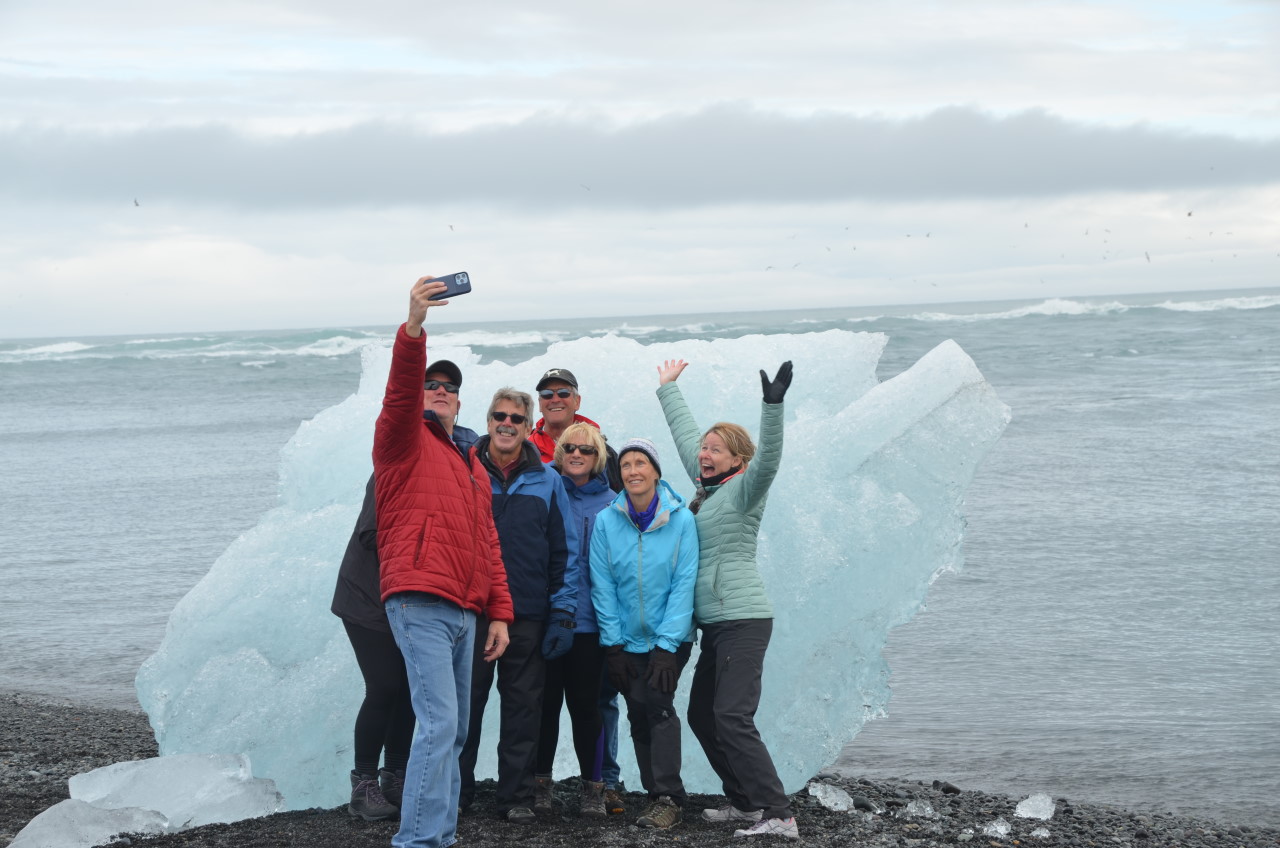 Sieben Touristen posieren am Diamond Beach Jökulsarlon für ein Handy Foto vor einem zwei Meter hohen Eisblock. 