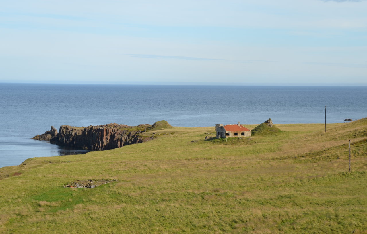 Blick auf eine Landzunge mit Meer, Haus und blauem Himmel in Island