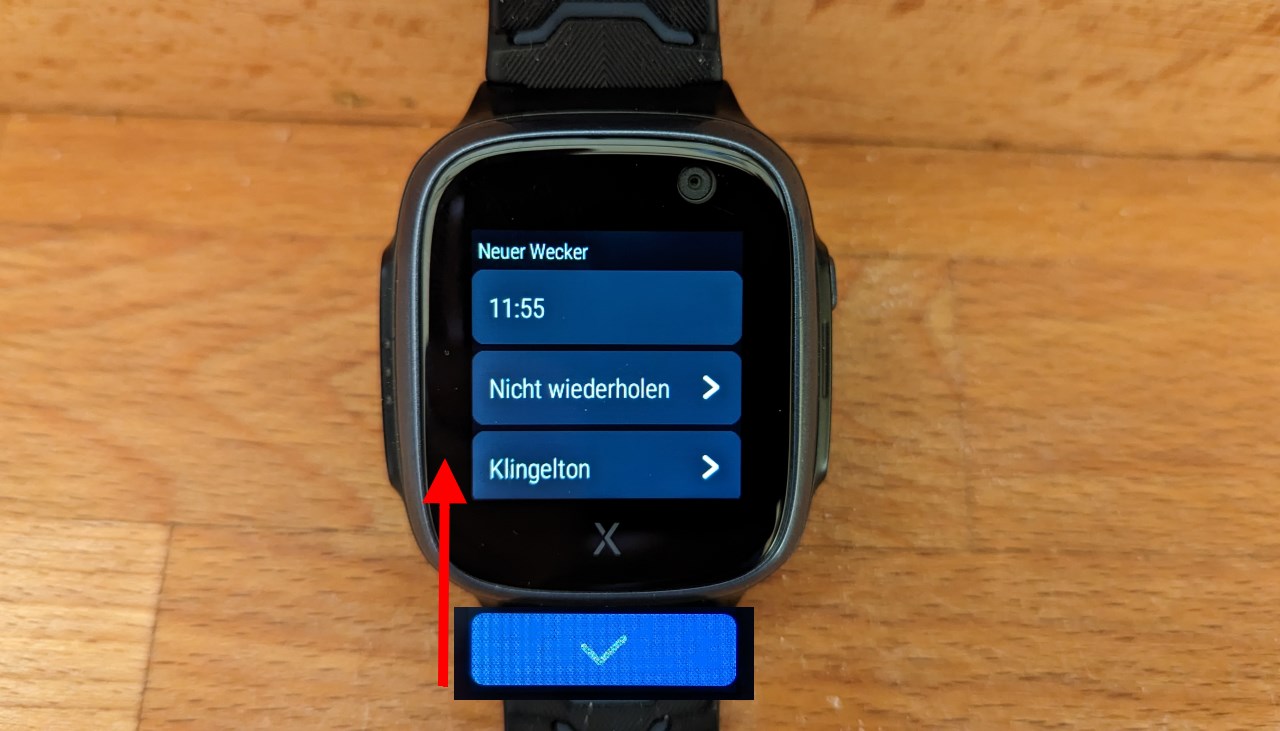 Foto einer Xplora x5 Smartwatch vor braunem Hintergrund. Das Display zeigt die manuelle Eingabe für einen neuen Alarm. 