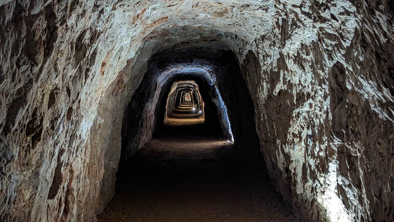 Blick durch einen langen in den Stein gehauenen Tunnel der von kleinen Lampen erleuchtet wird