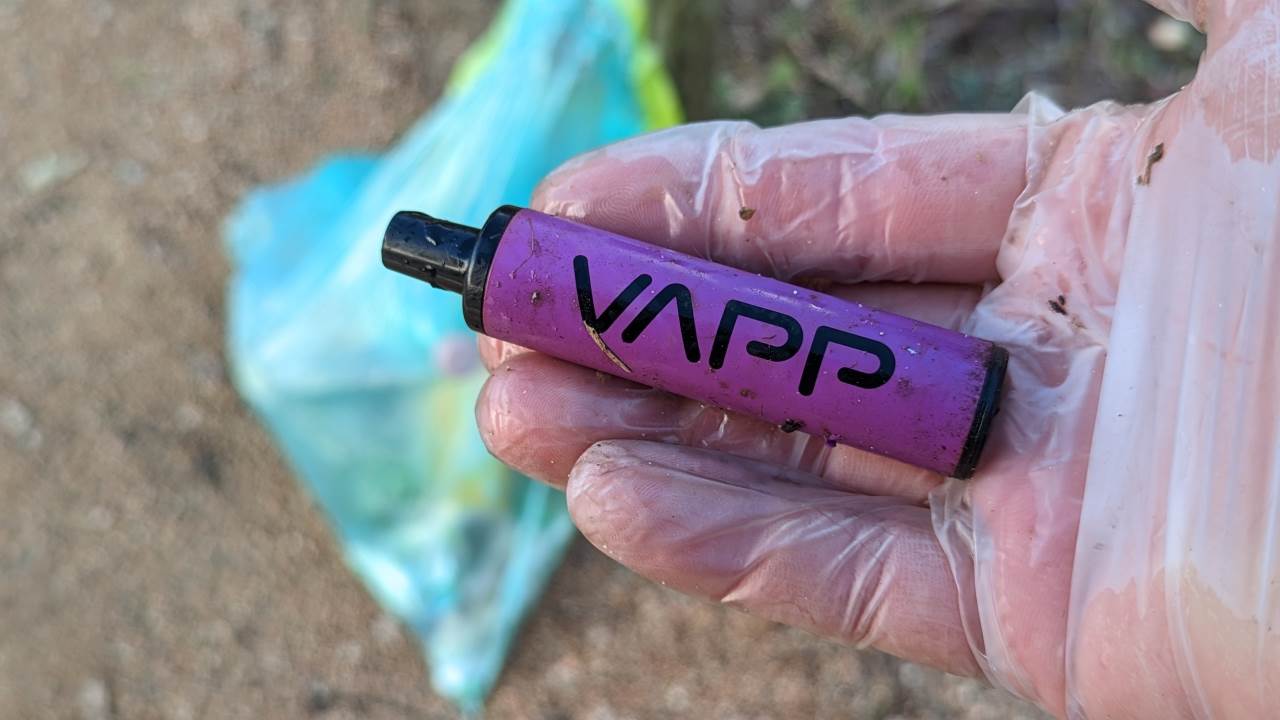 Eine Hand im Handschuh hält einen  weggeworfenen VAPP e-Zigarette Einweg Artikel. Elektroschrott in der Natur. 