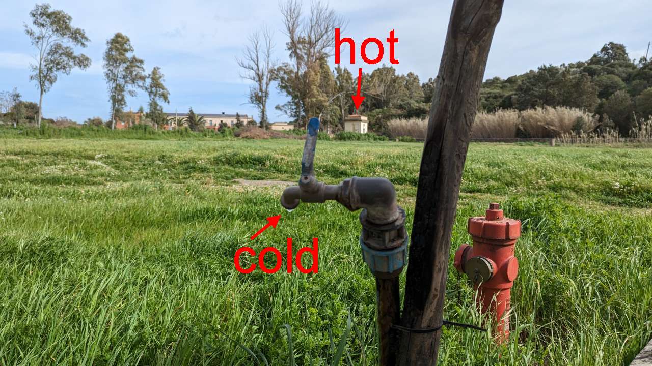 Die heisse Quelle in Sardara im Hintergrund als weisser Steinquarder, im Fordergrund ist ein Wasserhahn für kaltes Trinkwasser.