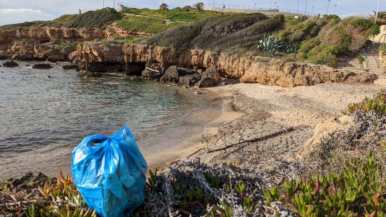 Blaue Tüte mit aufgesammelten Plastik Abfällen am Strand von Alghero Italien