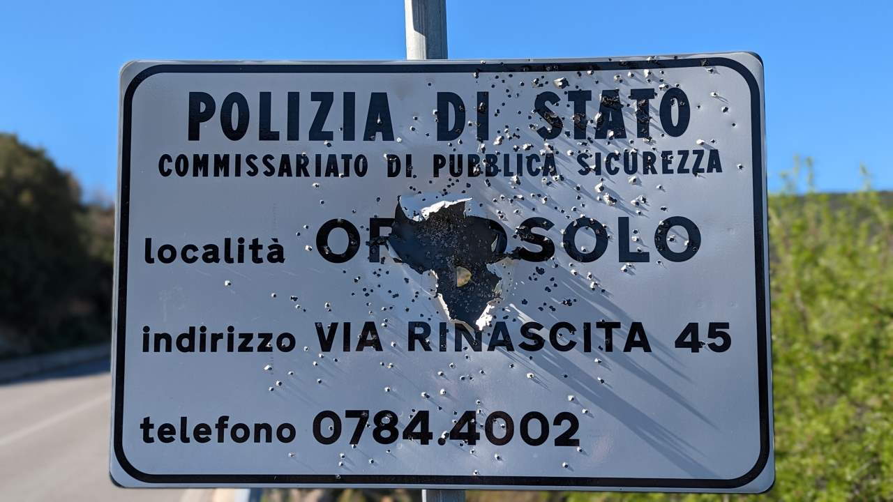 Von Kugeln zerstörtes Strassenschild mit der Aufschrift Polizia Di Stato localita Orgosolo und einer Telefonnummer