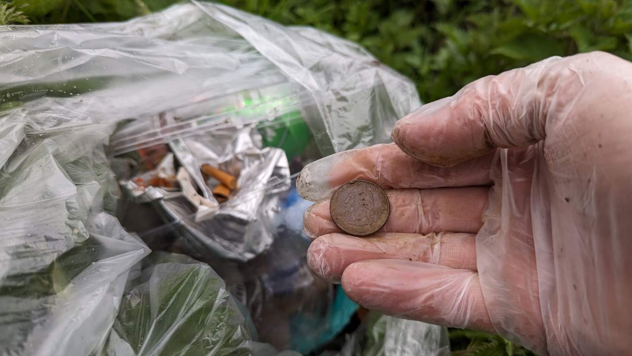 Eine Hand im Einweghandschuh zeigte eine 25 US cent Münze vor einer Tüte mit eingesammelten Müll