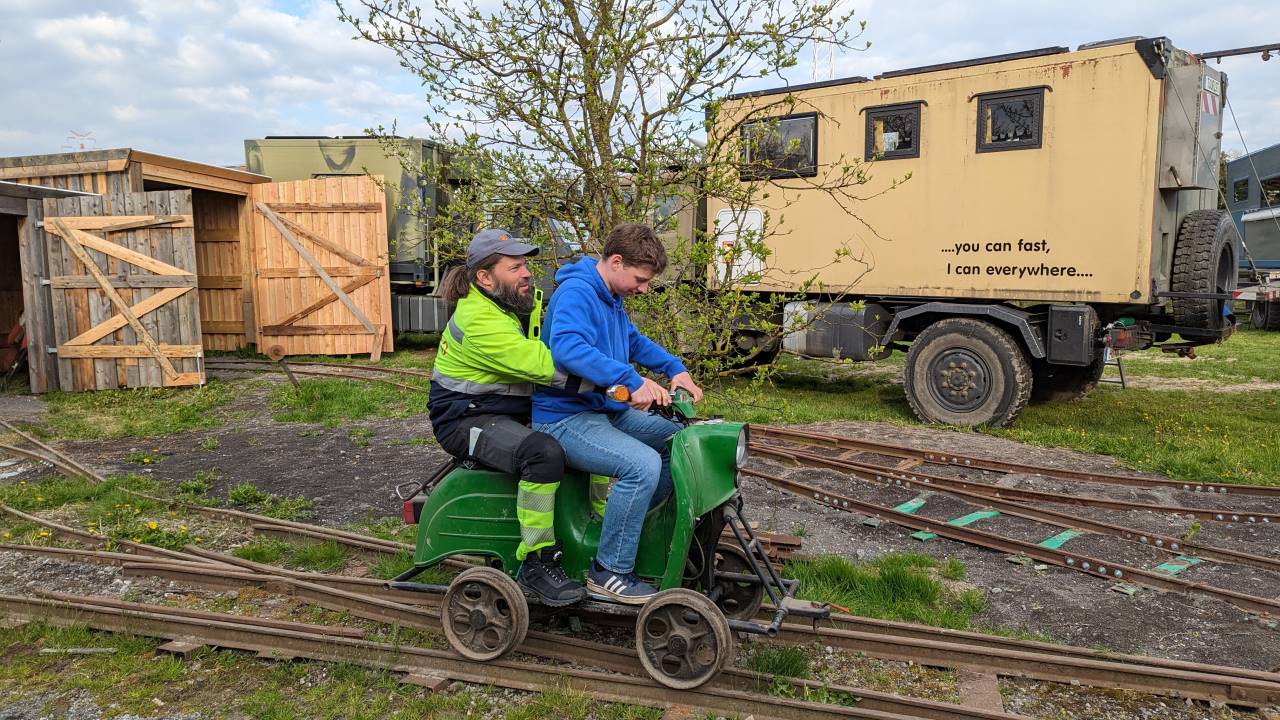 Zwei Personen fahren auf einer Draisine. Es sind mehrere Schalspurbahn Schienen zu sehen 