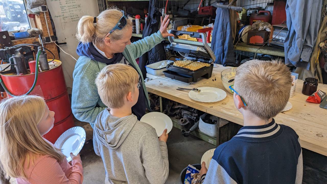 Drei Kinder warten mit leeren, weissen Tellern von einem aufgeklappten Waffeleisen mit einer frisch gebackenen Waffel
