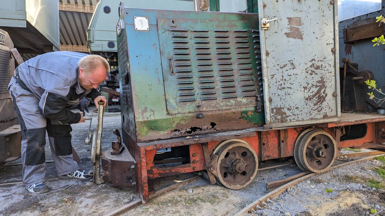 Eine entgleiste Feldbahn Lok wird von einem Mann mit einem Hebegeschirr angehoben und zurück auf die Gleise gesetzt