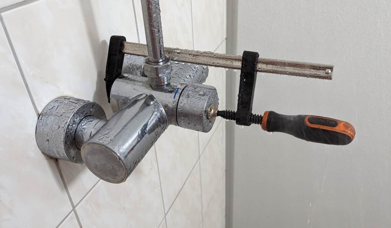 Eine Schraubzwinge hält den Druckwasserknopf einer Dusche dauerhaft gedrückt