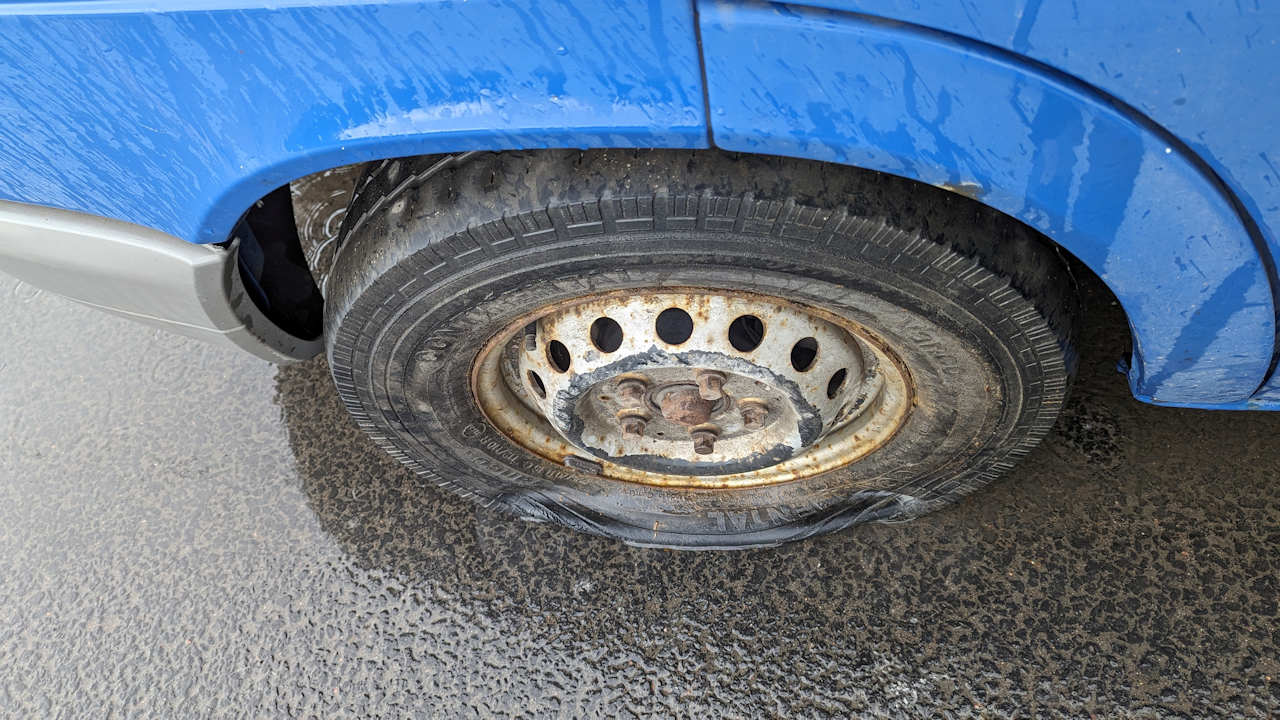 Völlig verbrauchter, platter Reifen ohne Profil an einem blauen Mercedes Kastenwagen im Regen