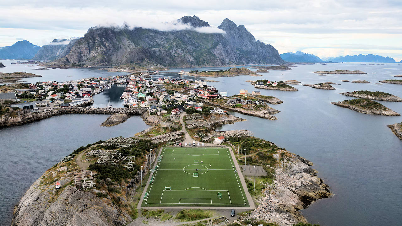 Luftbild von Henningsvaer Inseln mit dem berühmten Fußballplatz im Vordergrund und den Bergen im Hintergrund
