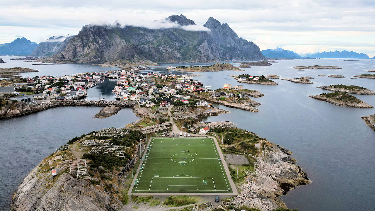 Luftbild von Henningsvaer Inseln mit dem berühmten Fussballplatz im Vordergrund und den Bergen im Hintergrund