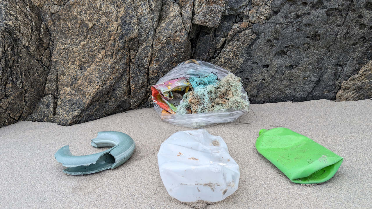angeschwemmter Plastik Abfall am Strand, teilweise im durchsichtiger Mülltüte