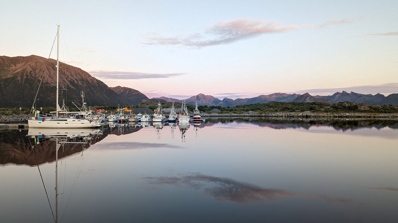 Im Hafen von Laukvika Lofoten spiegeln sich Boote und der Himmel im glatt liegenden Wasser 