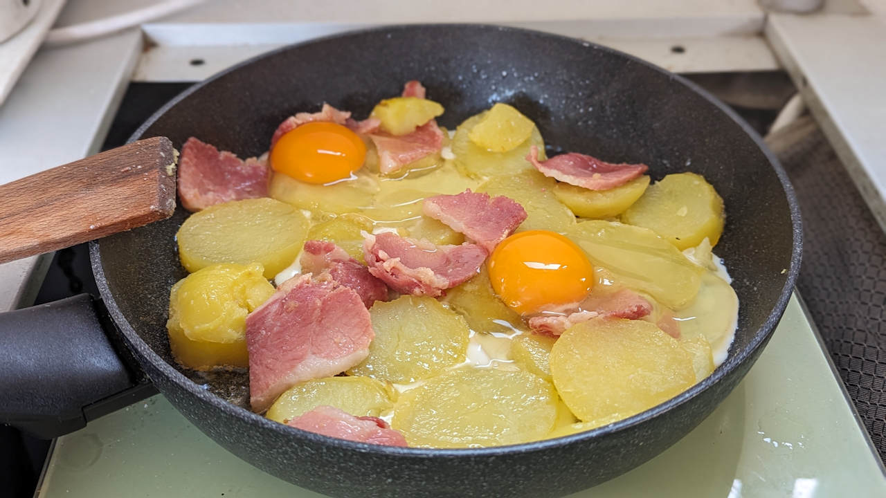 In einer Pfanne brutzeln Kartoffeln, Schinken und zwei Eier