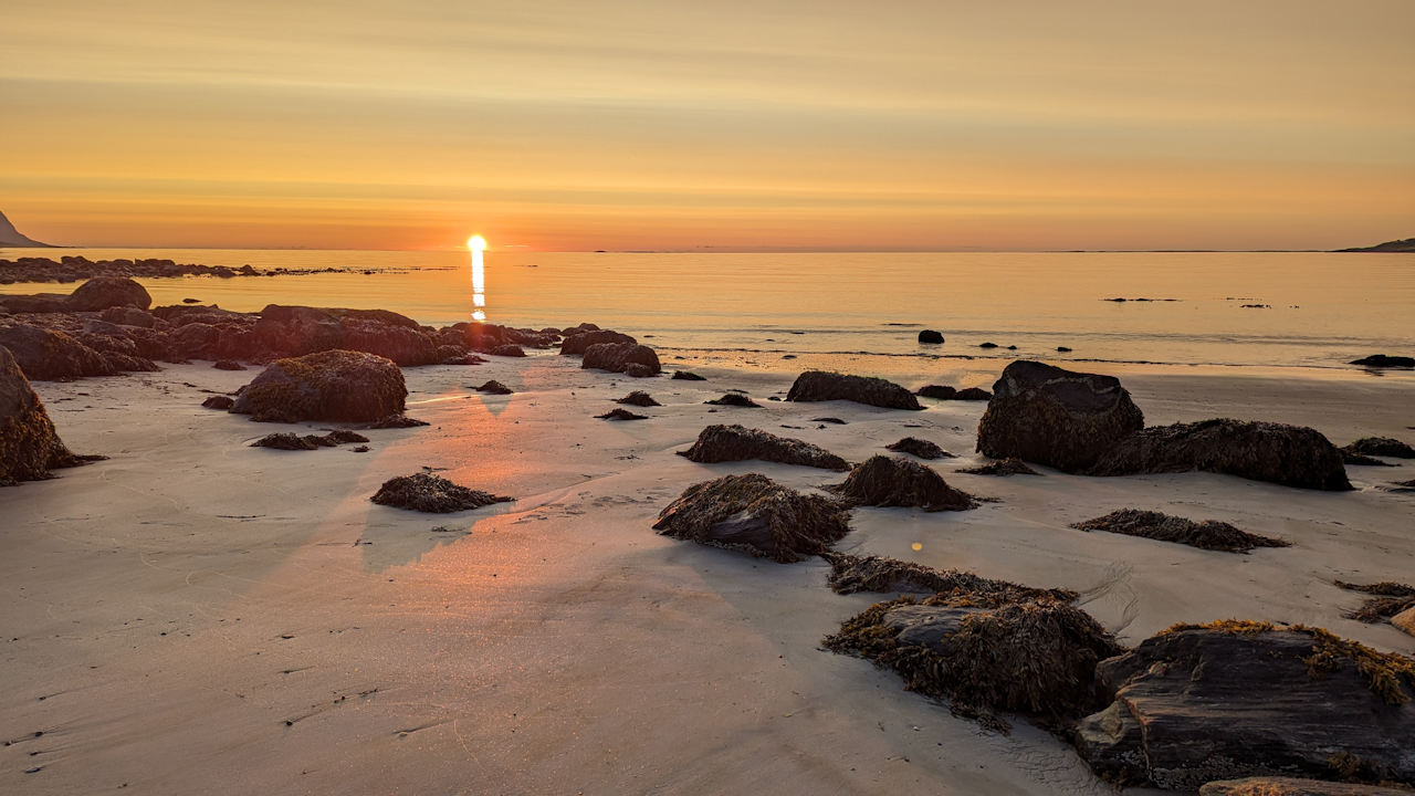Stimmungsvoller Sonnenuntergang an einem Strand mit Felsen in Norwegen