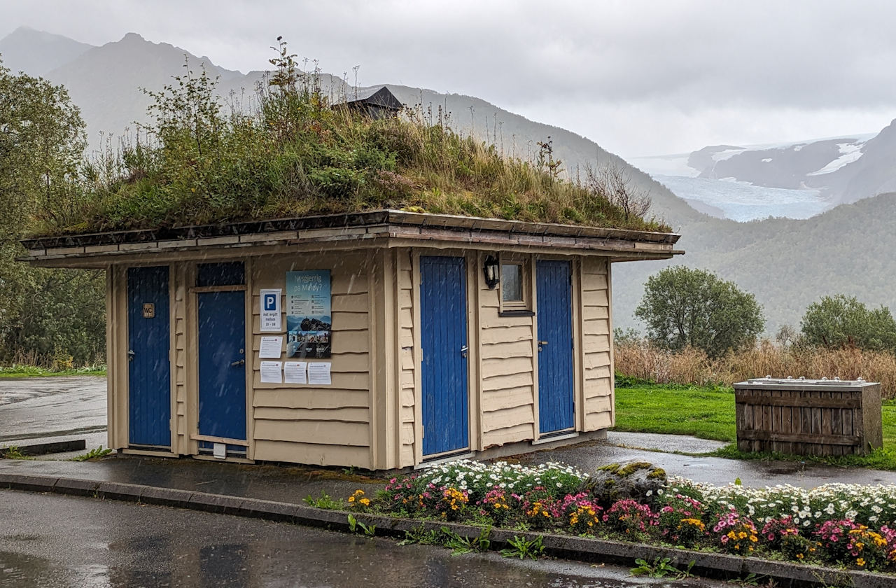 Klo Haus in Norwegen mit Blumenbeet und grün bewachsenem Dach