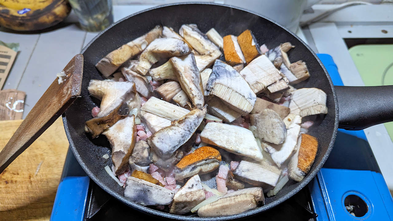 Pilzstücke und Speck brutzeln in einer Pfanne