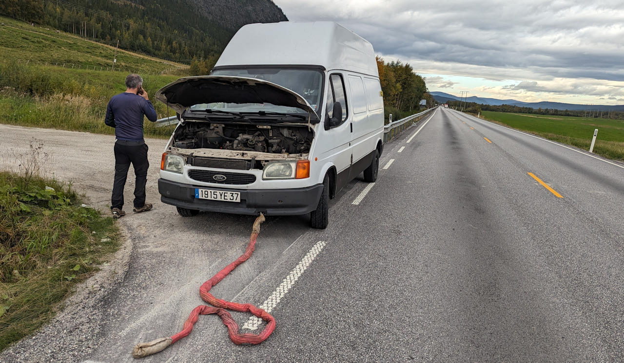 Ein Fahrer steht neben einem weissen Kastenwagen mit geöffneter Motorhaube und telefoniert. Am Fahrzeug ist ein Abschleppseil befestigt. 