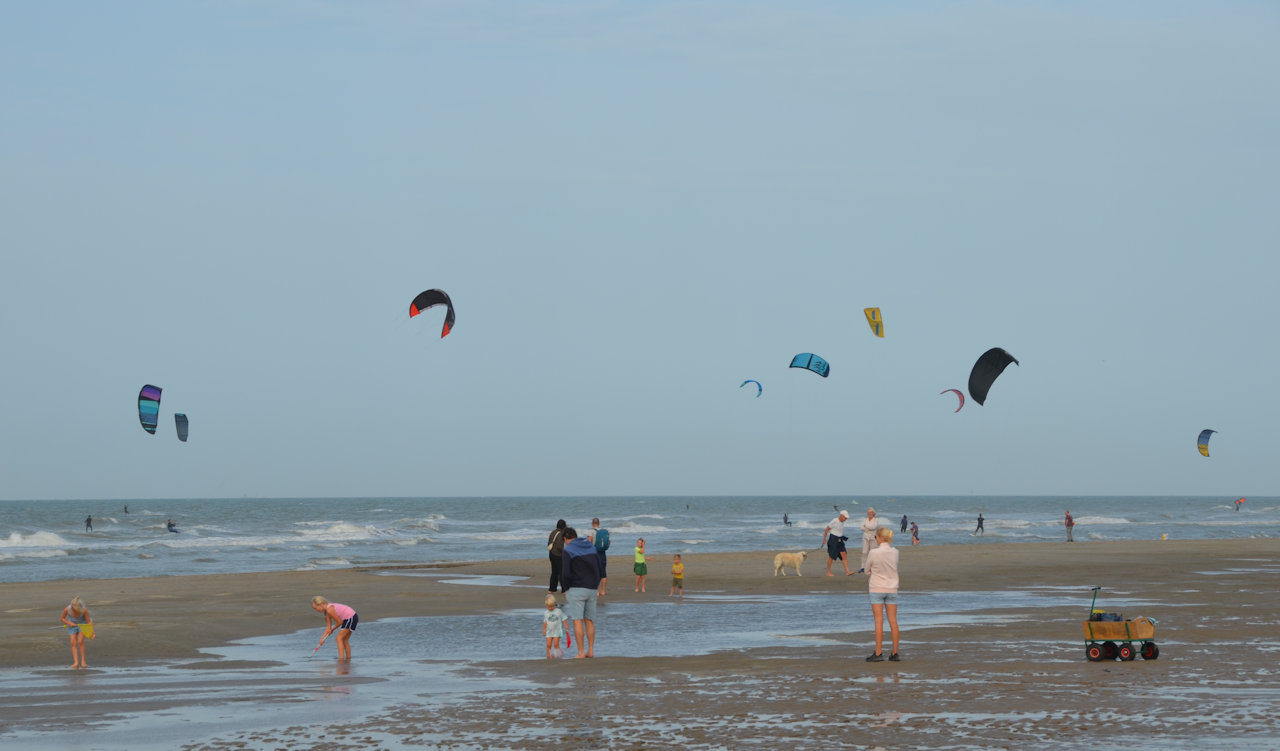 Kinder und Erwachsene und Kitesurfer am Strand von De Haan