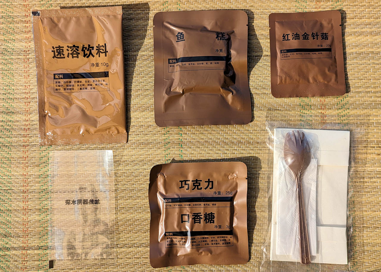 Inhalt von einem chinesischen MRE. Fischkuchen, Schokolade und Getränkepulver in braunen Tüten verpackt. 