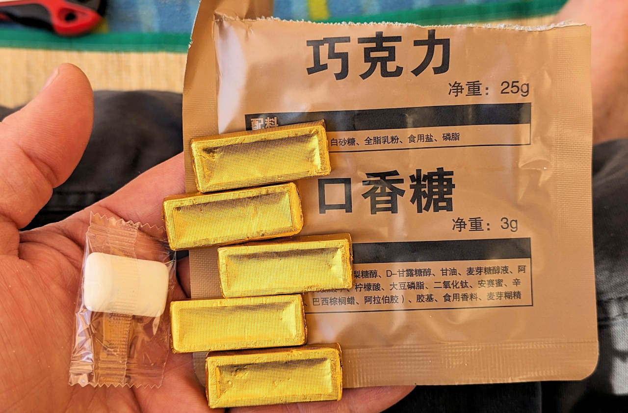 Inhalt von einem chinesischen MRE. Fünf kleine Portionen in goldener Folie verpackte Schokolade und ein weisses Kaugummi