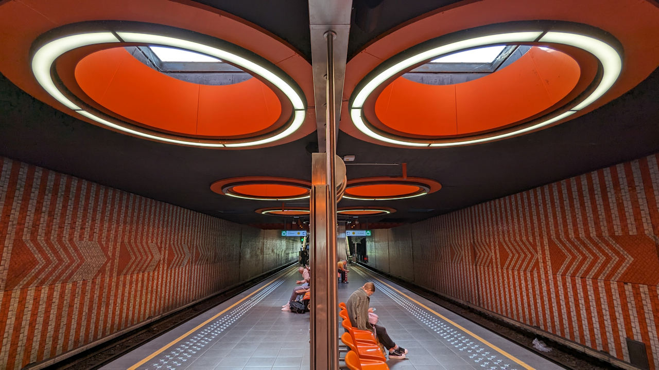 Bahnsteig der Metro Station Pannenhuis in Brüssel mit orangenen Wandmosaiken und Deckenlichtern